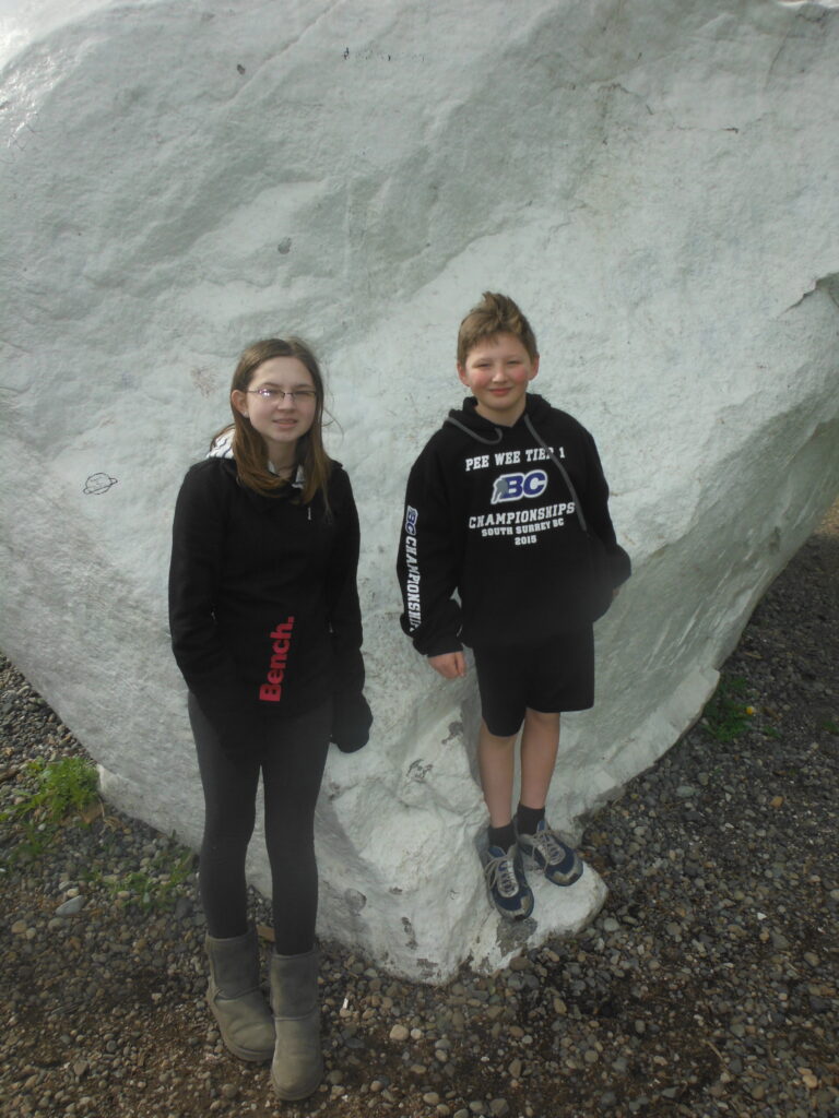 Image of two children standing in front of a painted white rock that is much larger than both of them