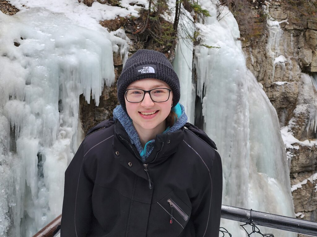 Image of a person in front of a cliff wall covered in ice.